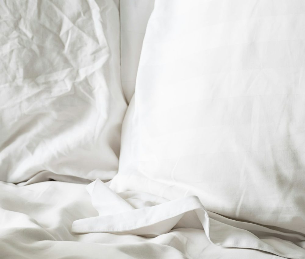 Soft white pillows on bedding, close up.